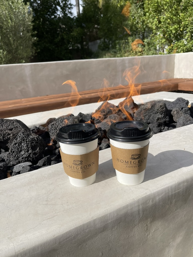 Two branded Homegrown coffee cups beside an outdoor fire pit