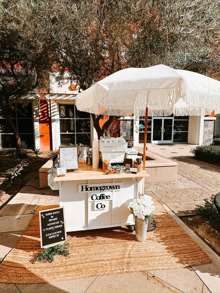 Homegrown mobile coffee cart beneath a fringed umbrella at an outdoor event