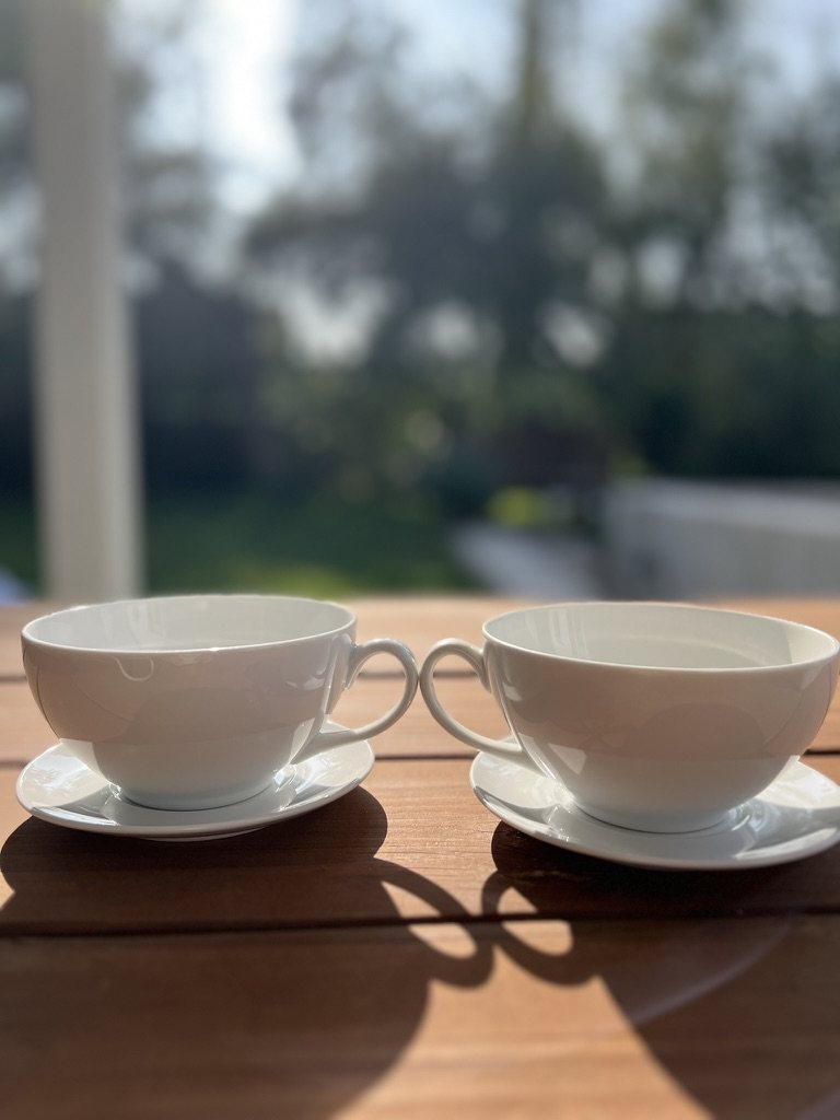 Two white coffee cups in warm afternoon sunlight