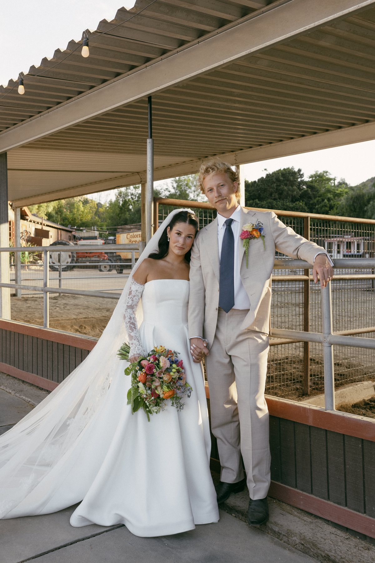 Newlyweds posing together beside a ranch railing