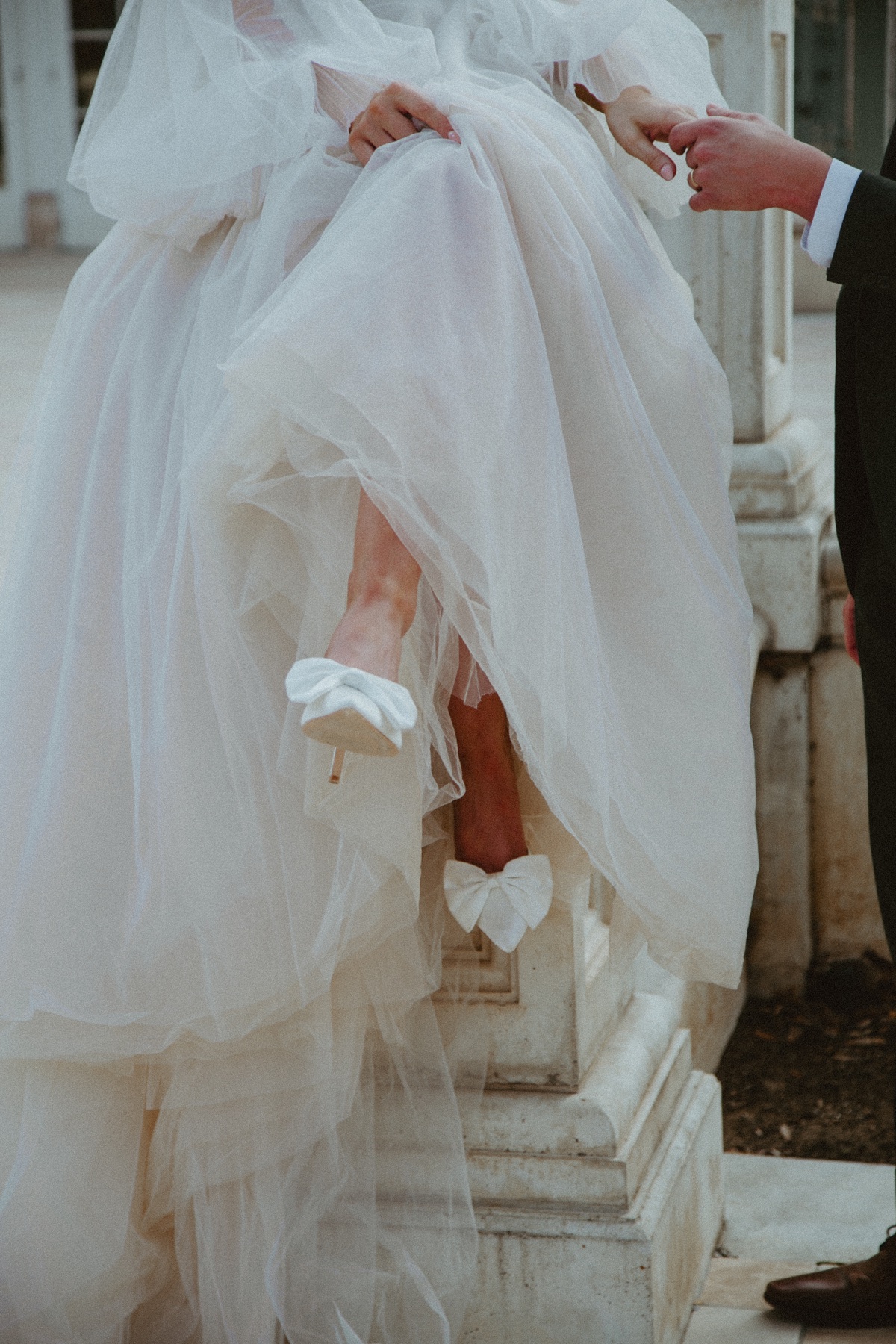 Bride lifting her gown to reveal bow-detailed wedding shoes